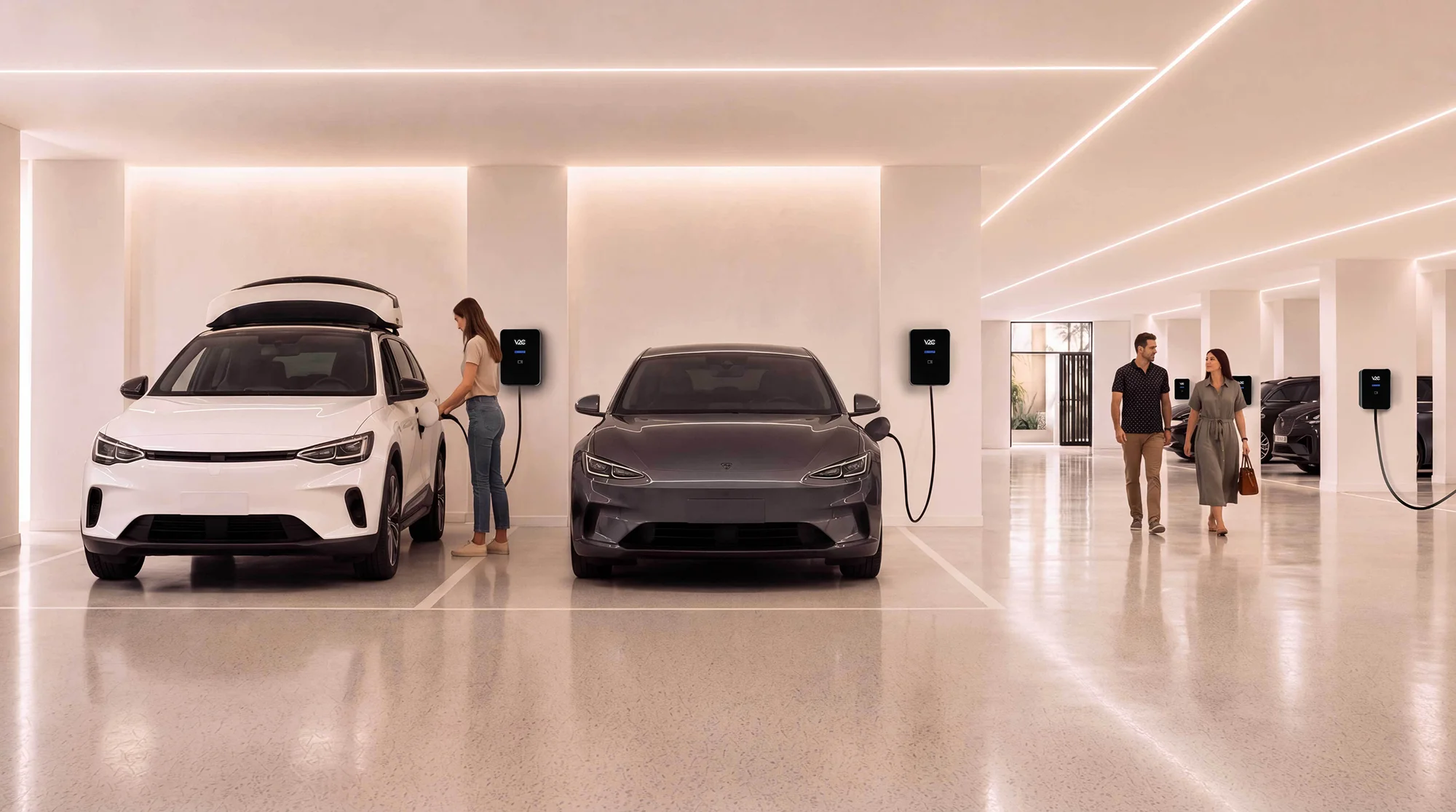 Una vecina enchufa su coche eléctrico al cargador de pared de su plaza en un garaje comunitario, con otro coche cargando en la plaza contigua, dos vecinos que pasan al fondo y más cargadores instalados en el resto de las plazas.